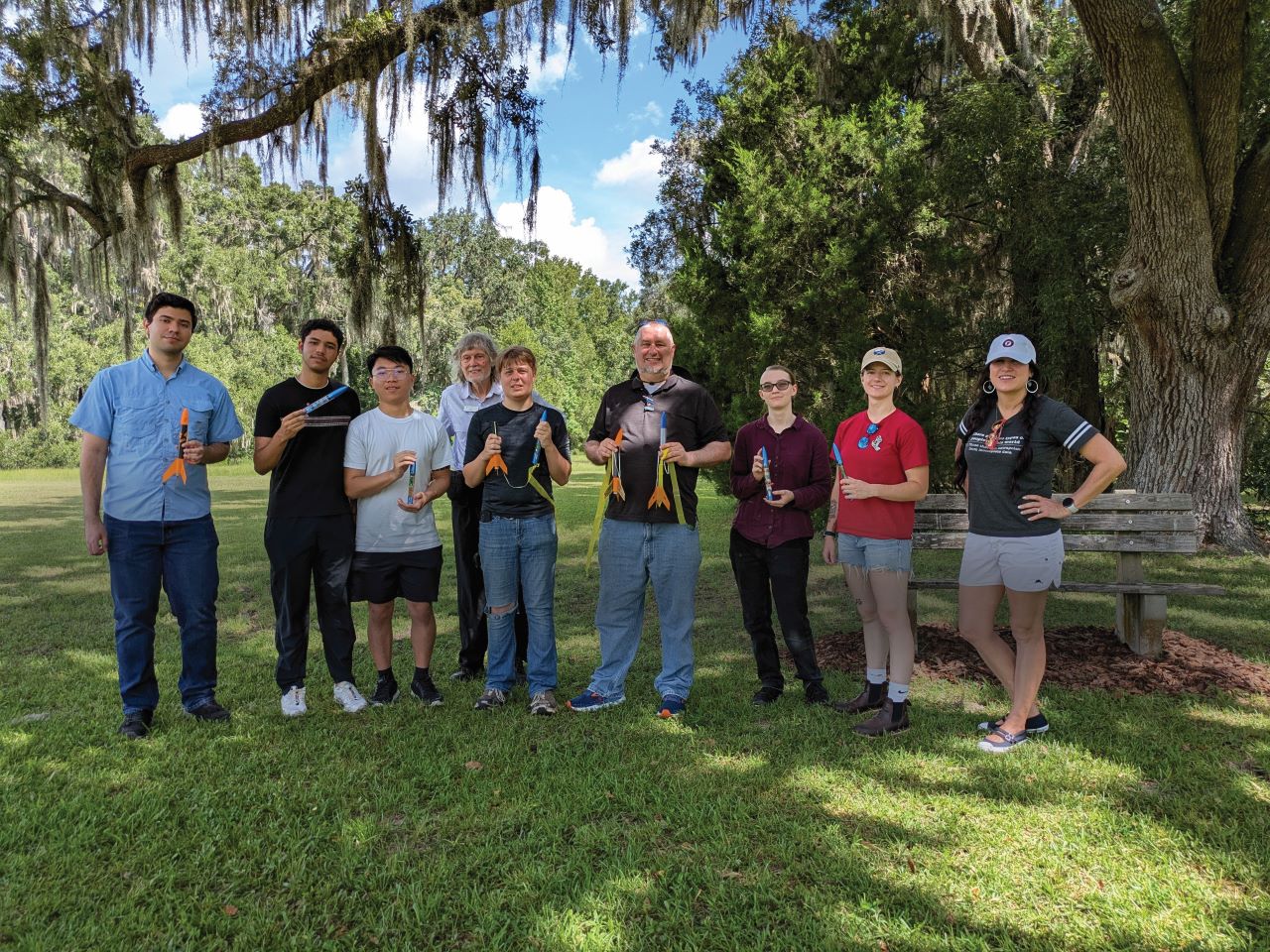 Several students and teachers hold toy rockets while standing in a field