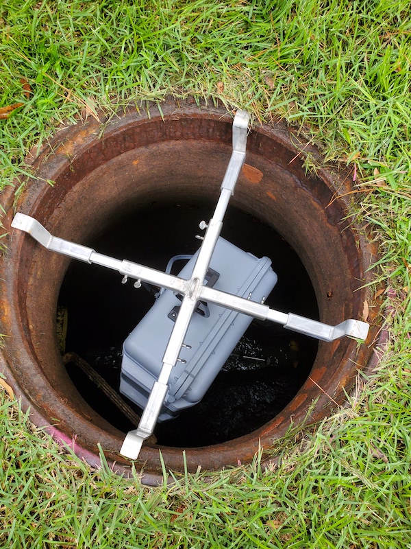 a plastic box that samples wastewater hangs in a manhole 