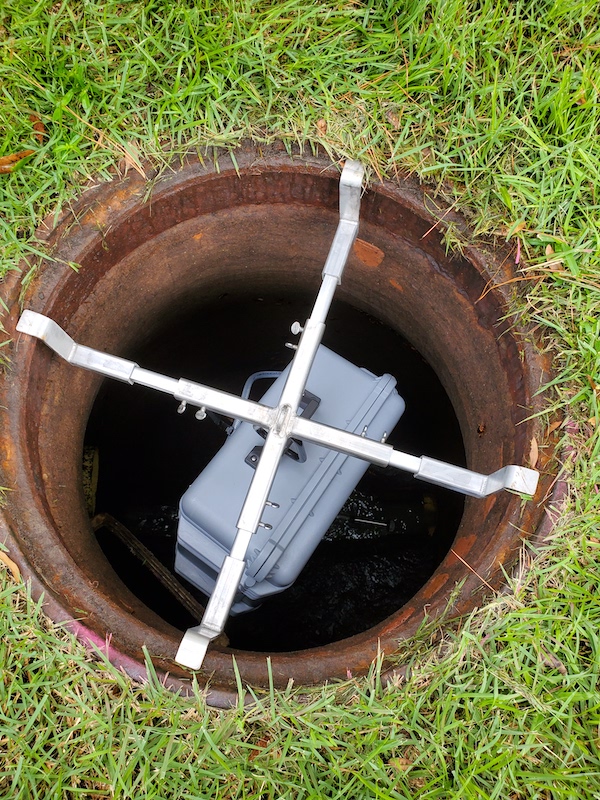 a plastic box that samples wastewater hangs in a manhole