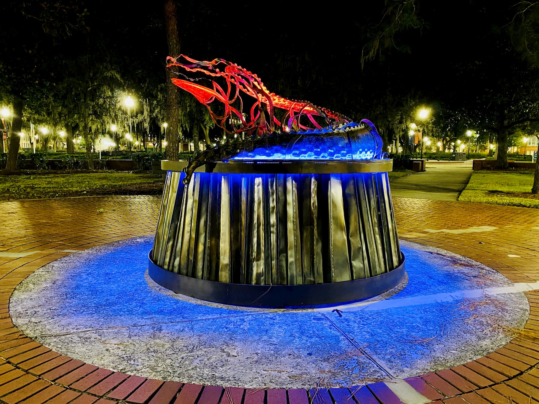A metal statue of an alligator at night illuminated with orange and blue lights