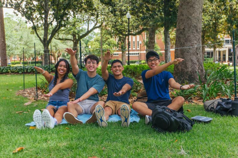 Four University of Florida students pose for a picture, gesturing the gator chomp, while sitting on the lawn of Plaza of the Americas during the first day of Summer B on Monday, June 29.