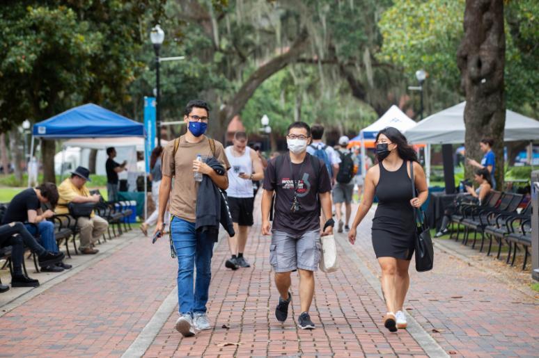 Three students wearing protective face masks walk along the University of Florida campus. 
