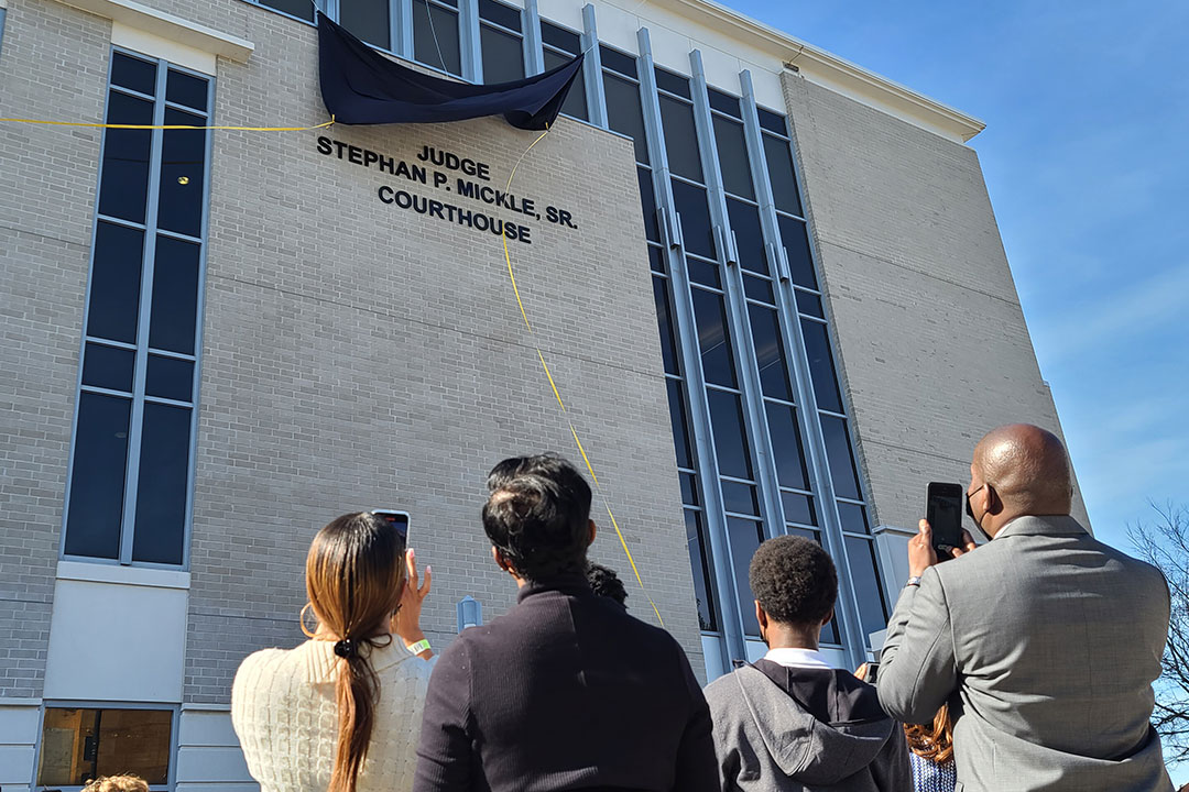 Several people stand as a curtain is lifted revealing the new name of the Alachua County Courthouse as the Judge Stephan P . Mickle, Sr., Courthouse