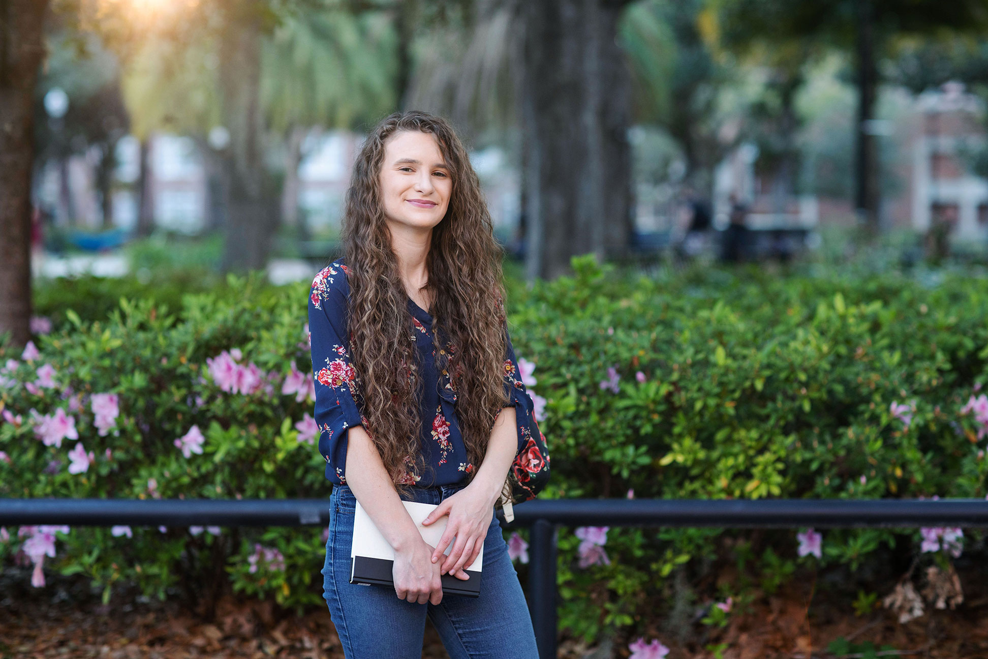 A woman stands in front of a bed of flowers while holding a book
