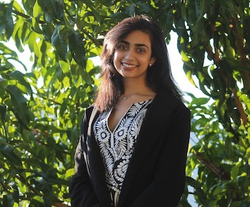 This is a portrait of a young woman standing before some trees.