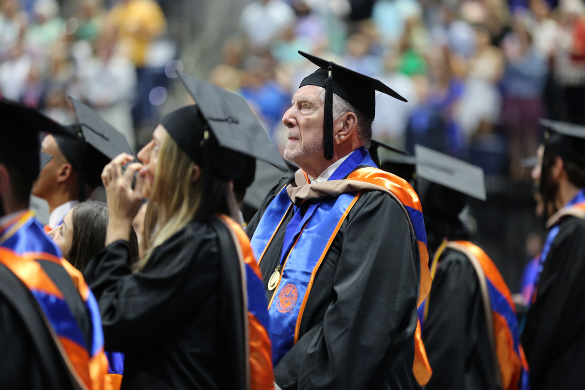 A man in graduation regalia standing at a commencement ceremony