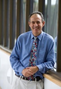 A man in a blue shirt with windows in the background.