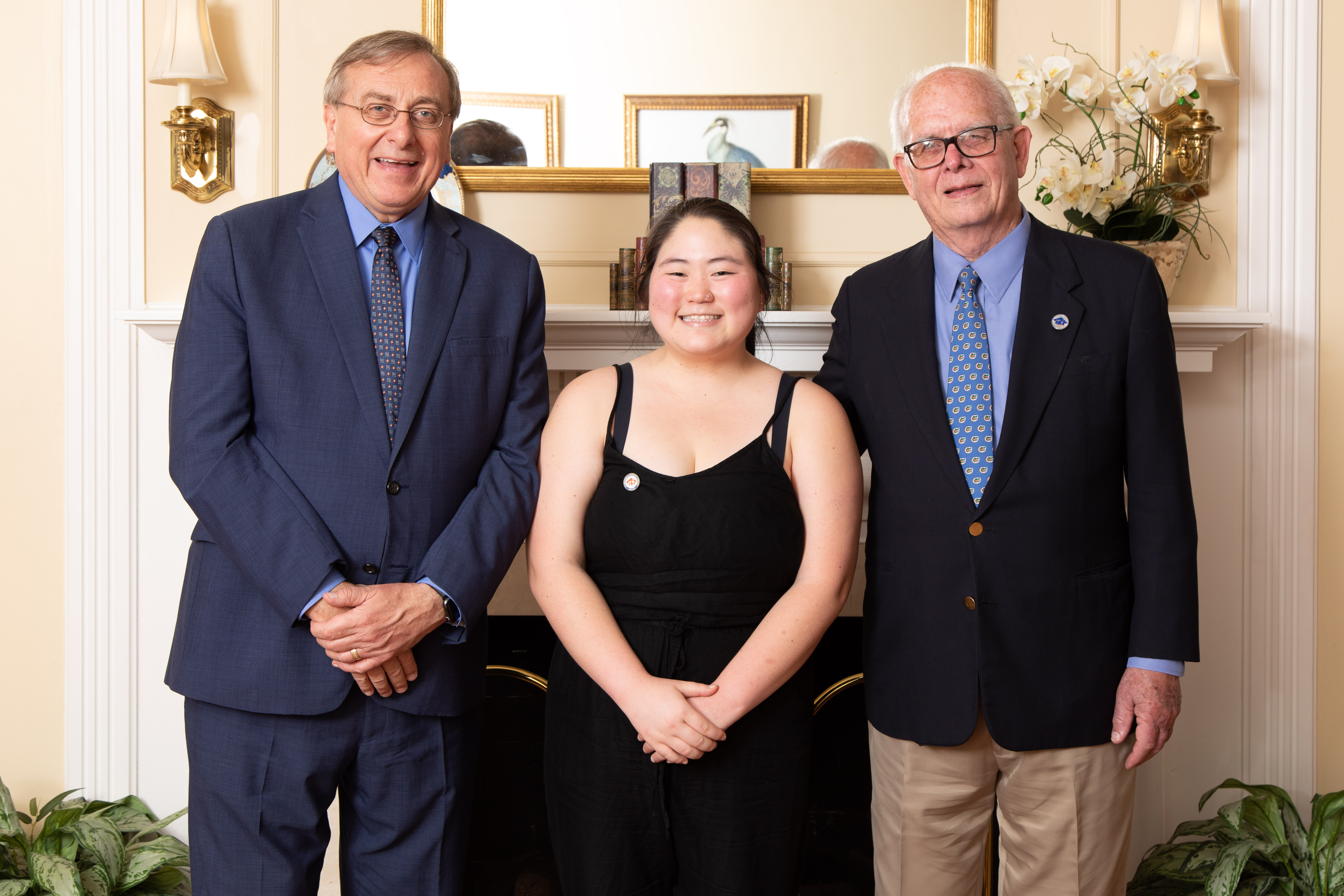 A woman and two men pose in front of a fireplace.