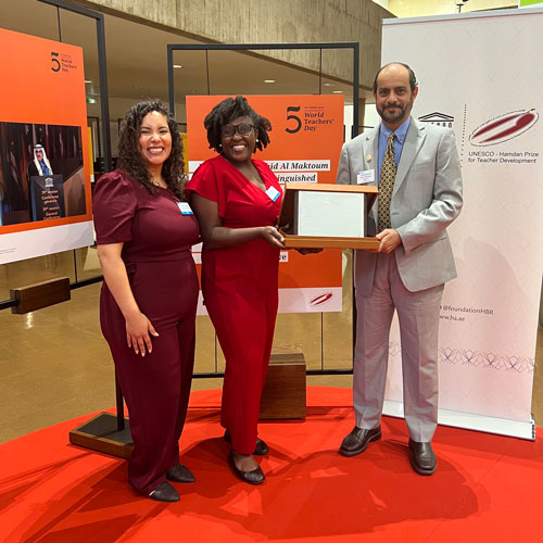 Two people accept an award from a person in a gray suit.