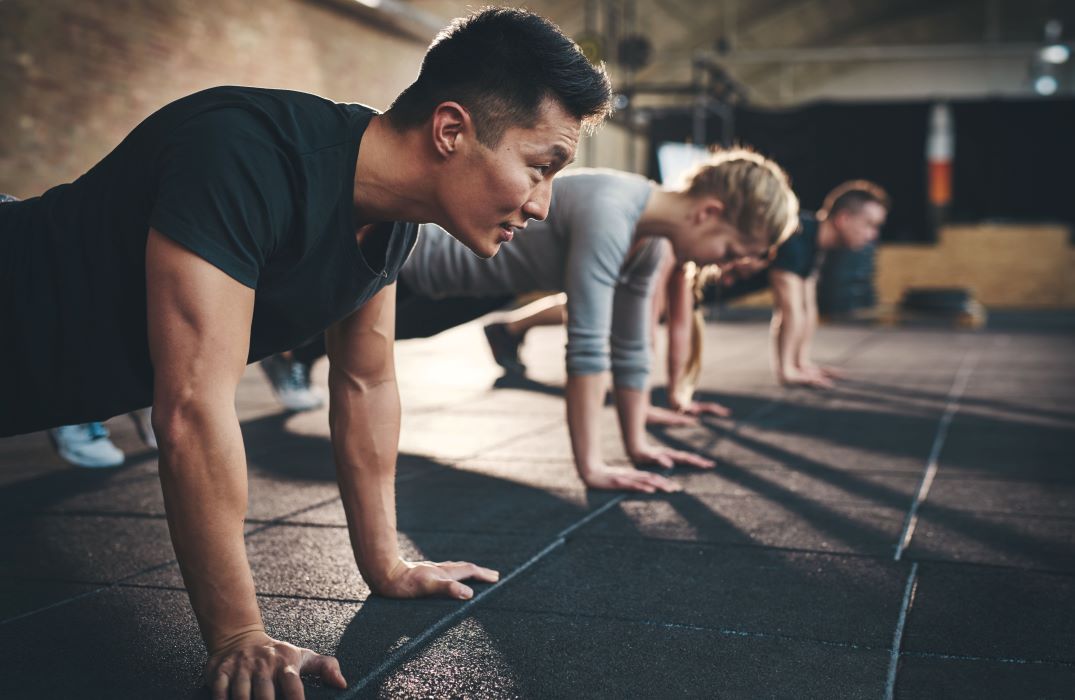 A man is at the top position of doing a push up in a gym with other people doing push ups in the background