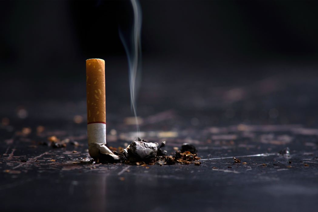 A cigarette crushed out on a black table with smoke wafting up