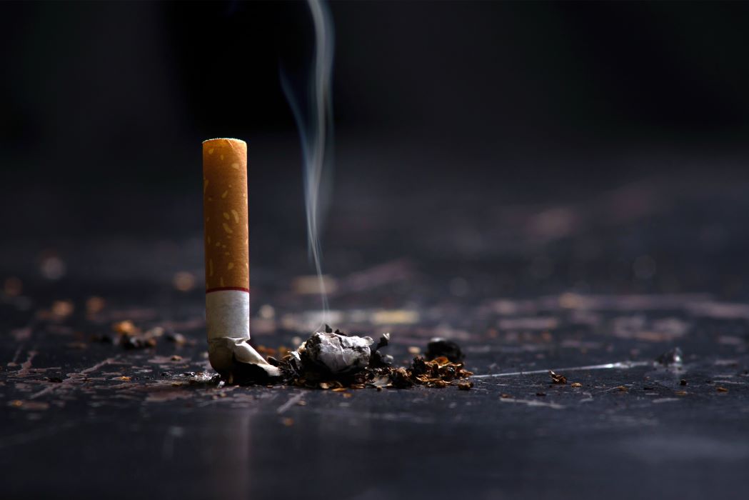 A cigarette crushed out on a black table with smoke wafting up
