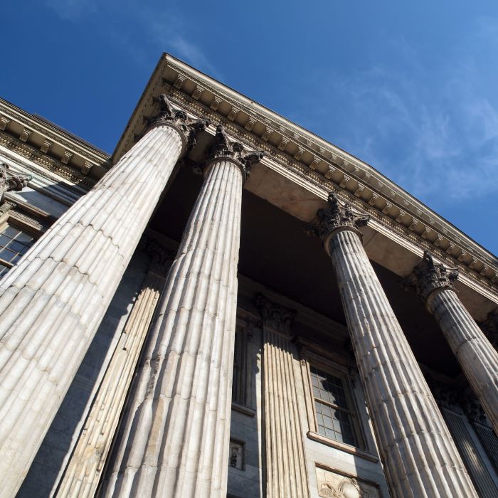 Looking up a steep angle at the ornate columns of a stone bank building with a blue sky above
