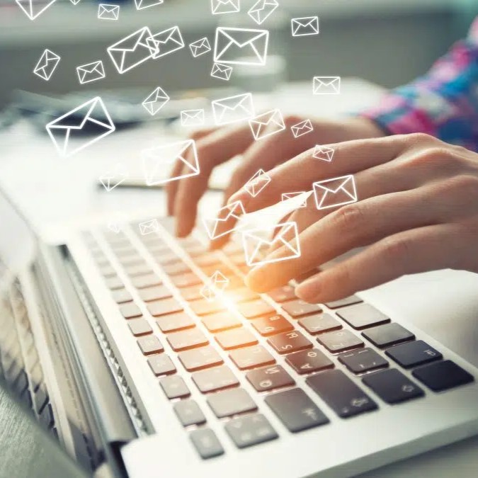 Fingers typing on a laptop keyboard as email symbols float above the computer