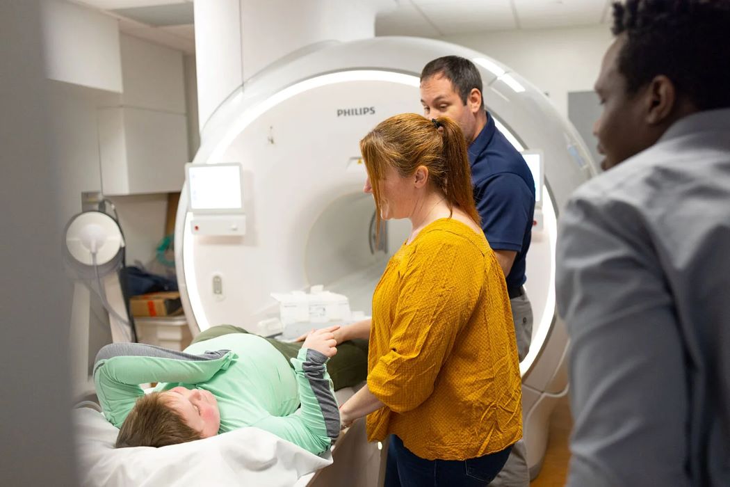 A young boy lying on an MRI table as adults look on and care for him
