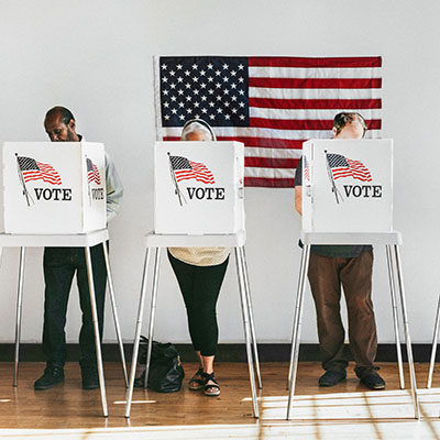 people behind voting booths with American flag in background
