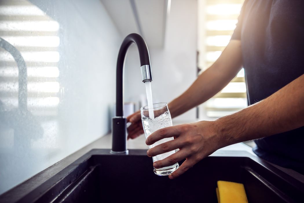 A man fills a water glass from a sink faucet
