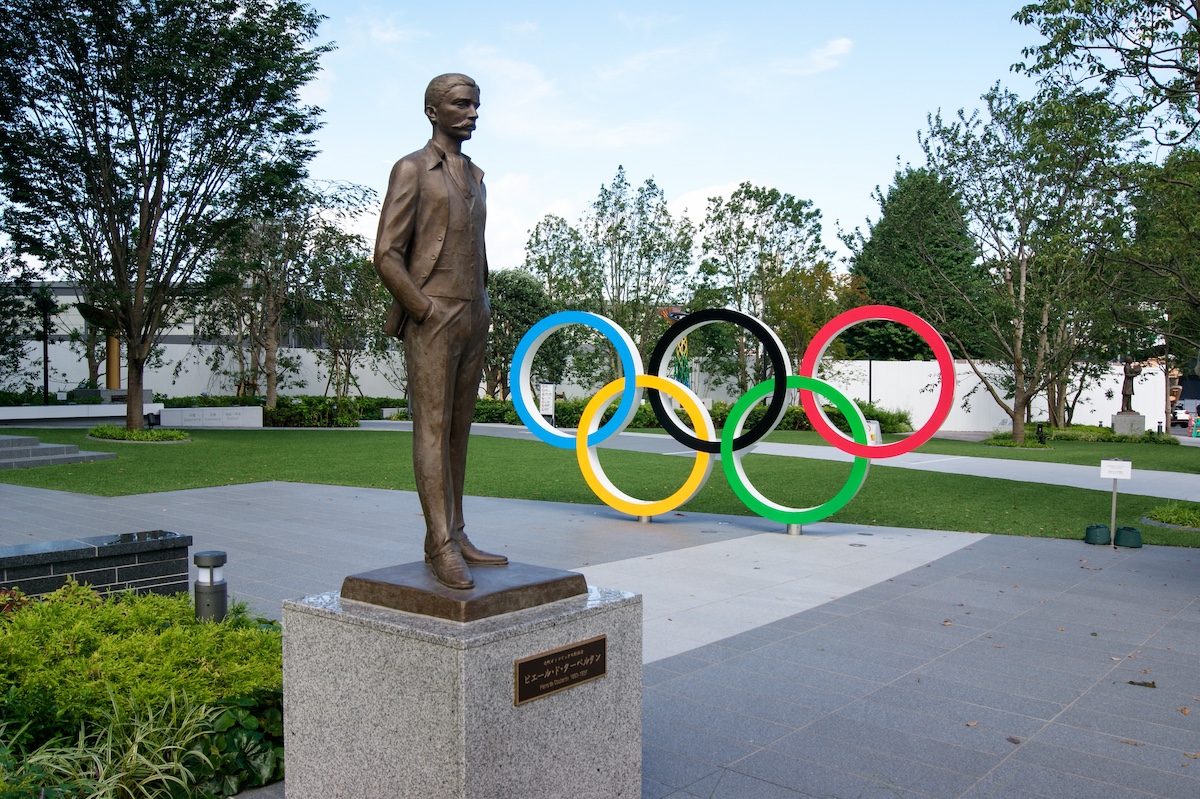 A statue of the father of modern olympics with the rings in background