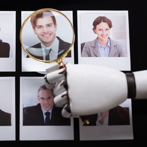 A robotic hand holds a magnifying glass over a set of six polaroid pictures of job candidates