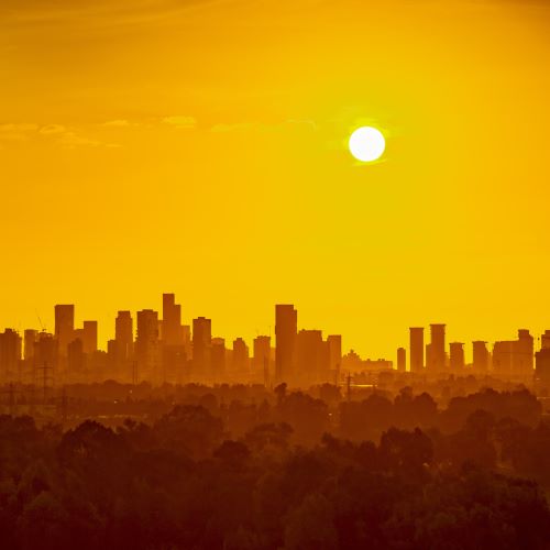 A city skyline in the distance with the sun shining in an orange hazy sky