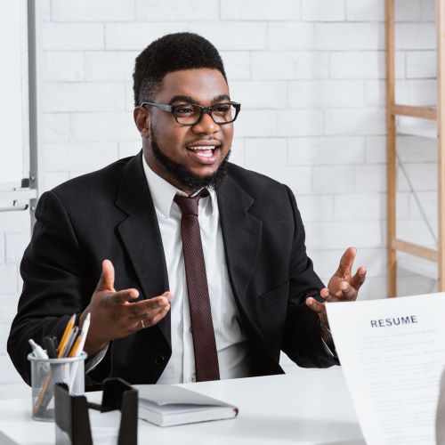 A job candidate sits at a desk and gestures toward a hiring manager