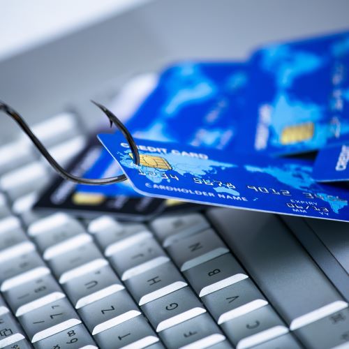 A fishing hook hooked onto a credit card above a laptop keyboard
