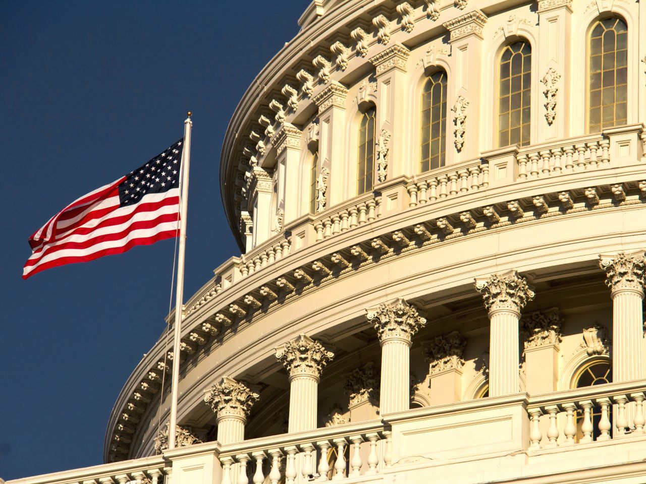 A close up view of the US Capitol dome with an American flag flying in front of it
