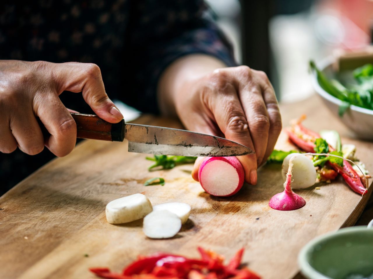 A close up view of a person slicing a radish on a wood cutting board