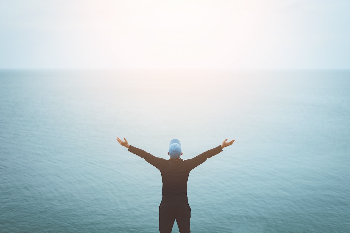 man raises hands in front of ocean