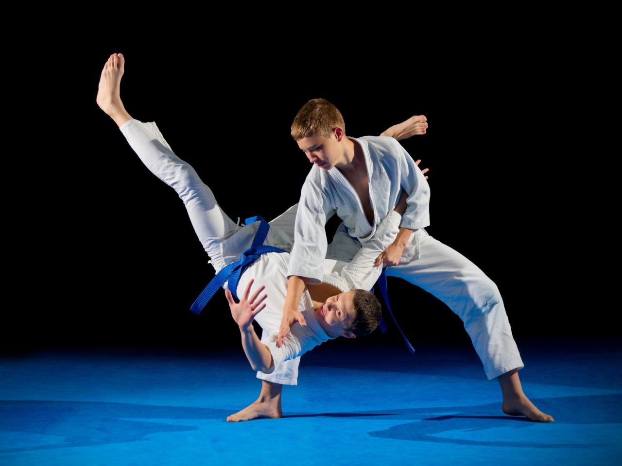 One young martial artist throwing another onto a blue mat