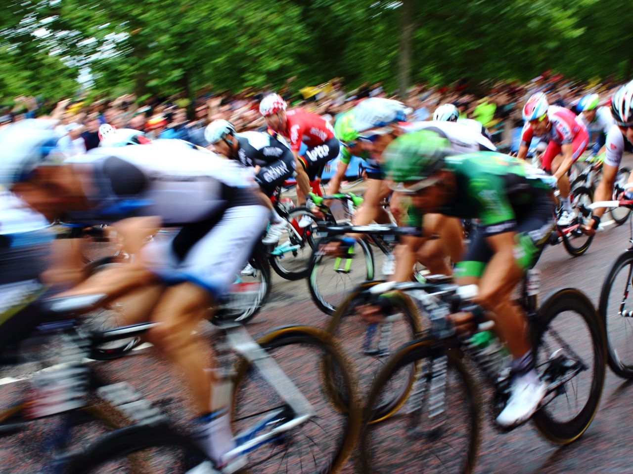 A motion-blurred image of many cyclists speeding down a roadway with spectators in the background