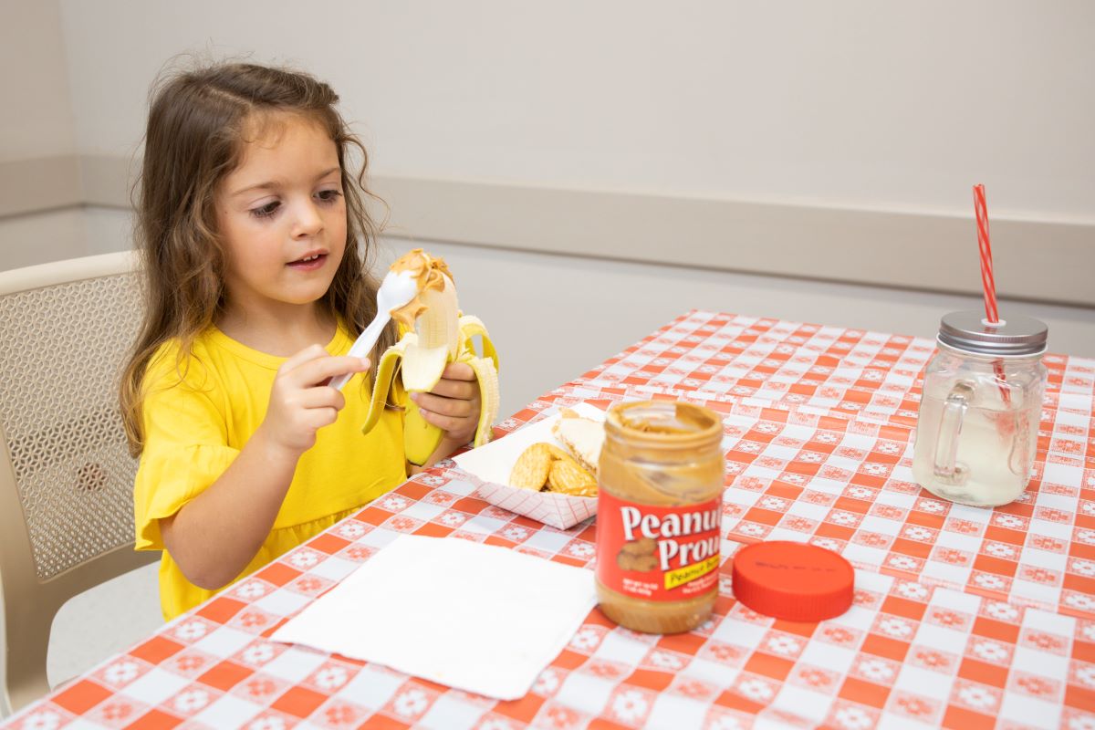 A young girl spreads peanut butter on a banana