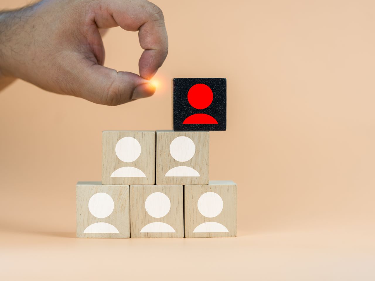 Blocks stacked into a period, with each block showing a profile of a person's face. A hand flicks off the top block from the pyramid
