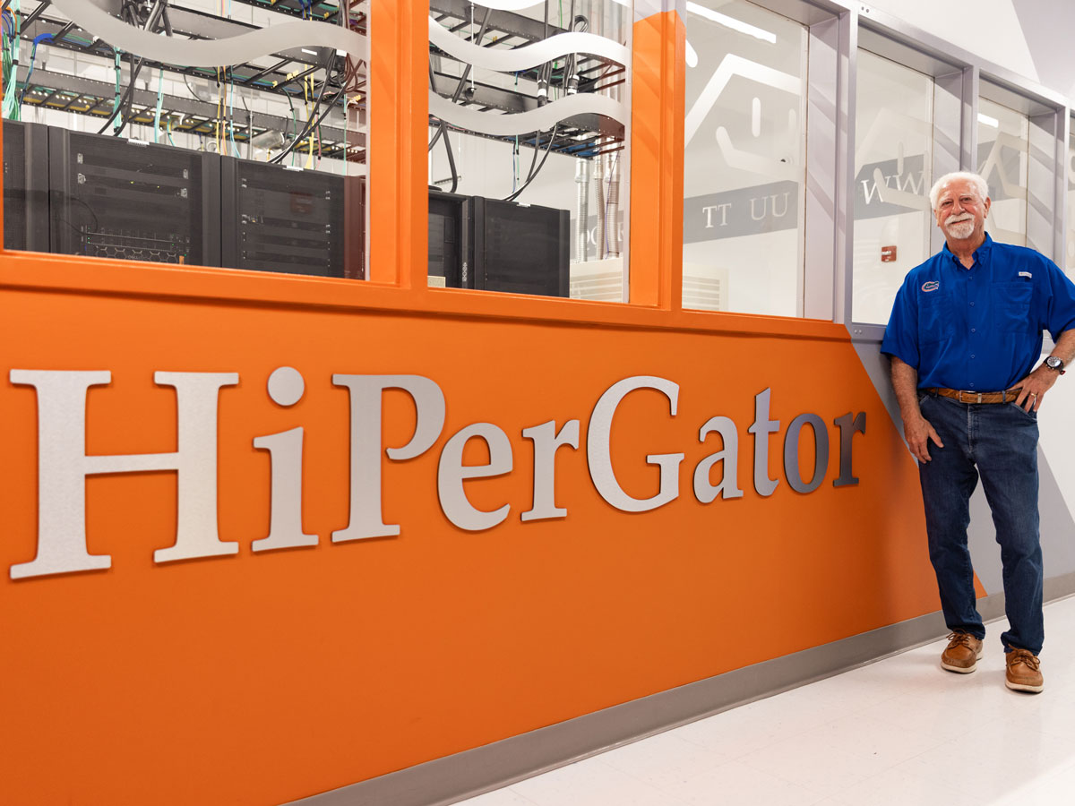 Chris Malachowsky stands next to an orange wall that says HiPerGator.