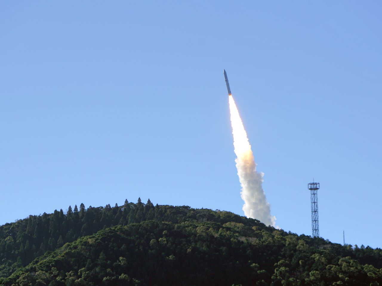 A rocket lifting off above a forested hill