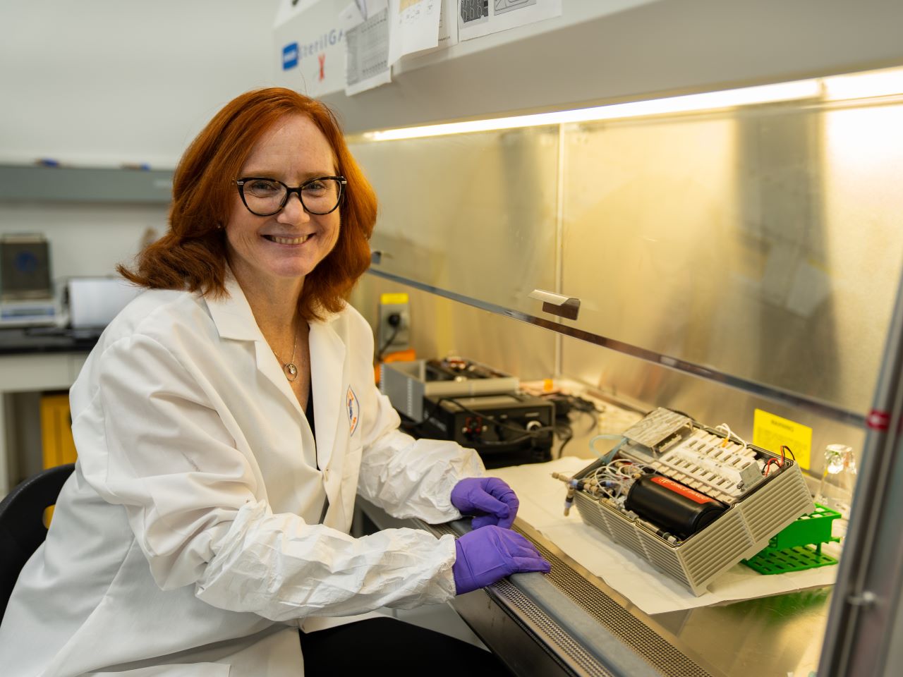 Siobhan Malany in a labcoat sits at a research bench and smiles at the camera