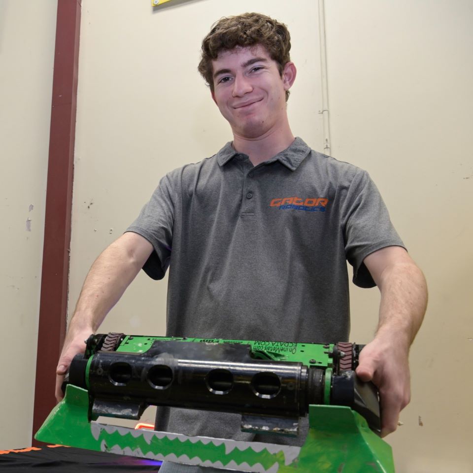 A college student holds a green battle robot up to the camera