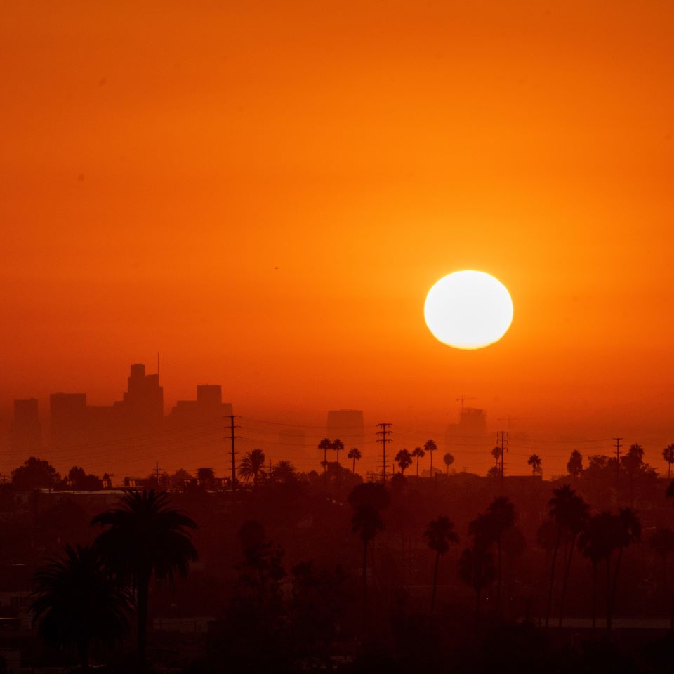 A bright sun against an orange sky above a hazy city scape